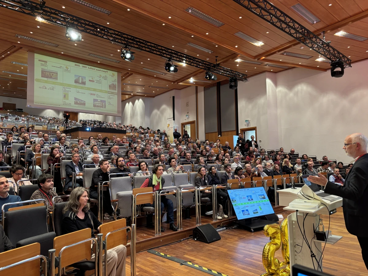 Referent spricht vor einem voll besetzten Hörsaal mit mehreren hundert Teilnehmenden. Auf einer großen Leinwand wird eine Präsentation gezeigt.