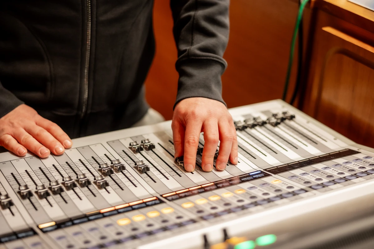Person bedient ein Mischpult mit Reglern und beleuchteten Tasten.