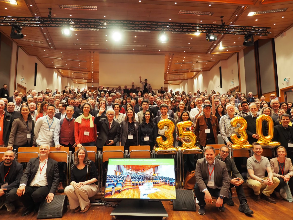 Gruppenfoto von zahlreichen Teilnehmenden einer Jubiläumsveranstaltung in einem Hörsaal. Im Vordergrund stehen goldene Ballons mit den Zahlen 35 und 30.